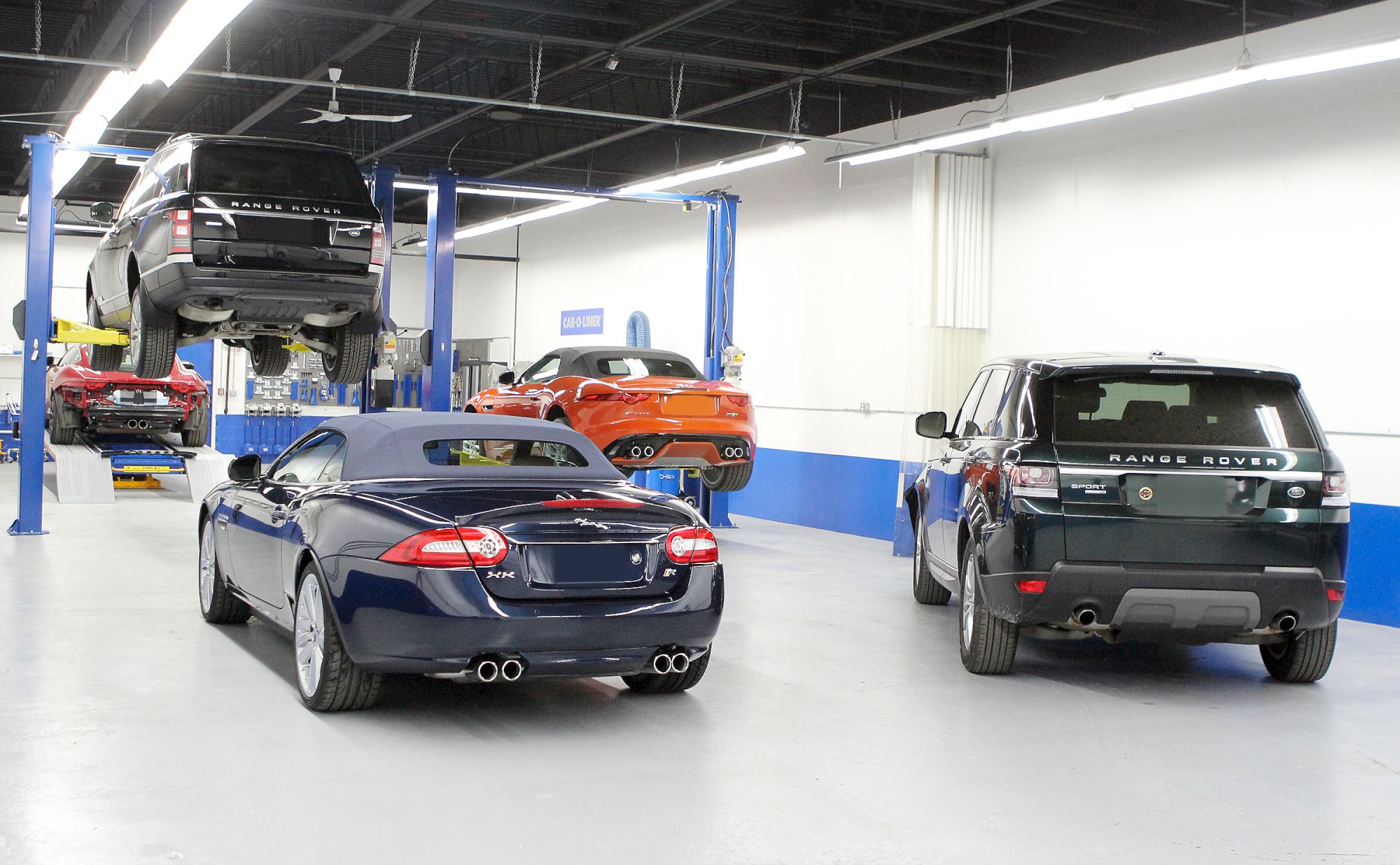 The image shows a car service garage with several vehicles, including SUVs and a convertible. Some cars are lifted for maintenance.