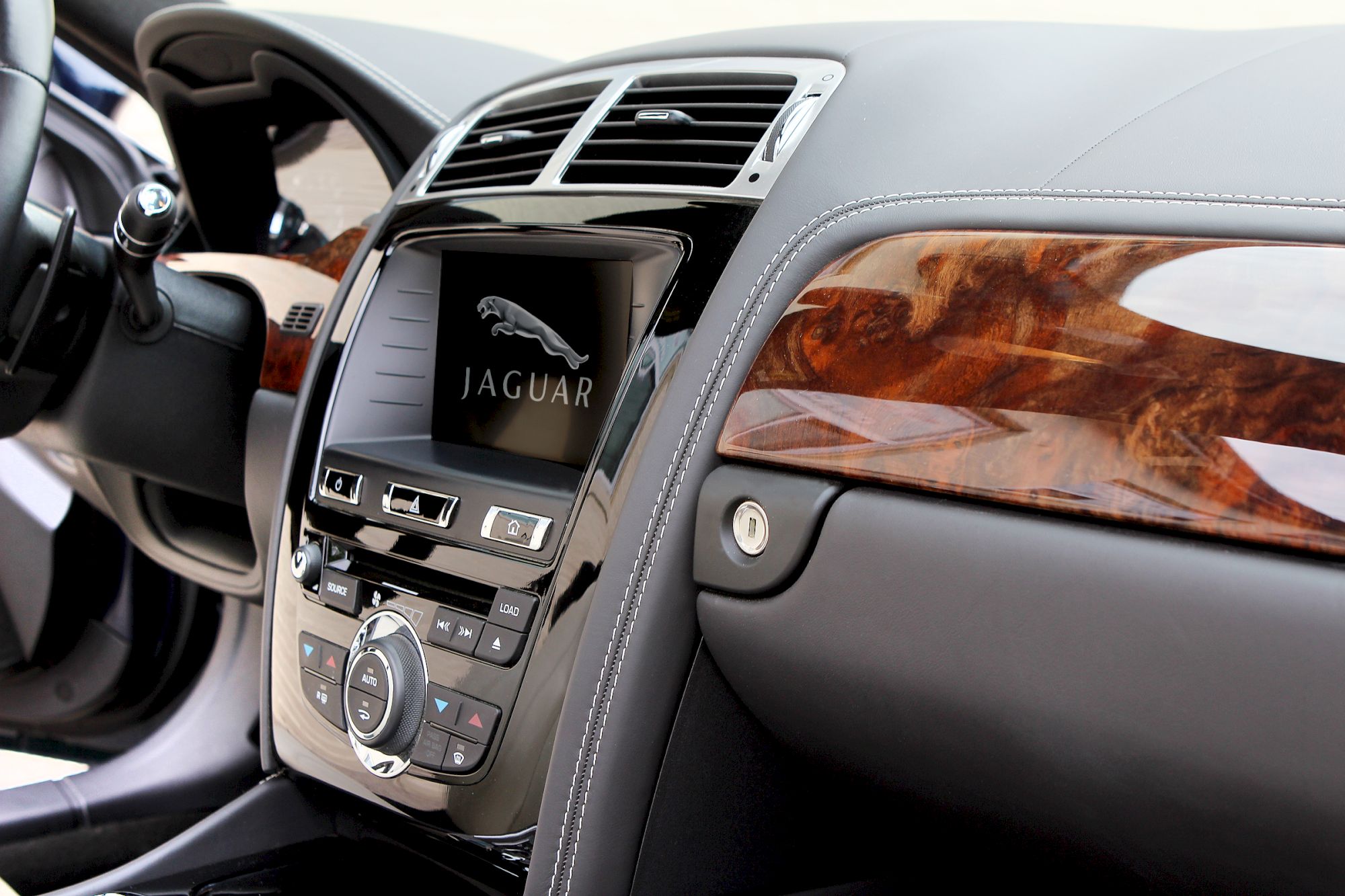 Car interior featuring a Jaguar logo on the display, wood accents, and sleek controls on the dashboard.
