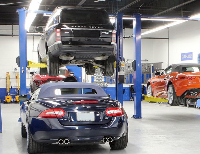 A car repair shop with vehicles on hydraulic lifts, one is elevated. Multiple cars are in the garage, indicating ongoing maintenance.