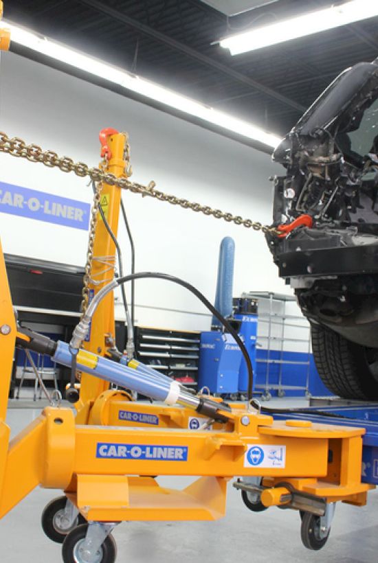 A car frame alignment machine in a garage setting with a vehicle mounted for repair.