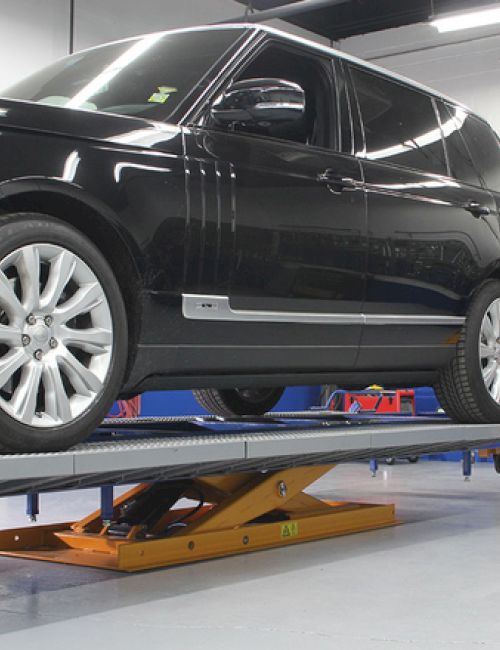 A black SUV is on a car lift in a garage, ready for maintenance or inspection.