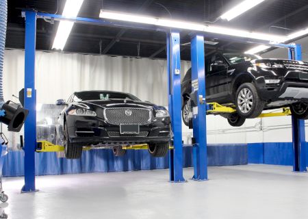 Two cars are elevated on hydraulic lifts in a brightly lit auto service shop, ready for maintenance or repairs.