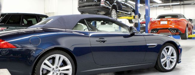 The image shows a car workshop with multiple vehicles, including a blue convertible and an SUV on a lift, and other cars in the background.