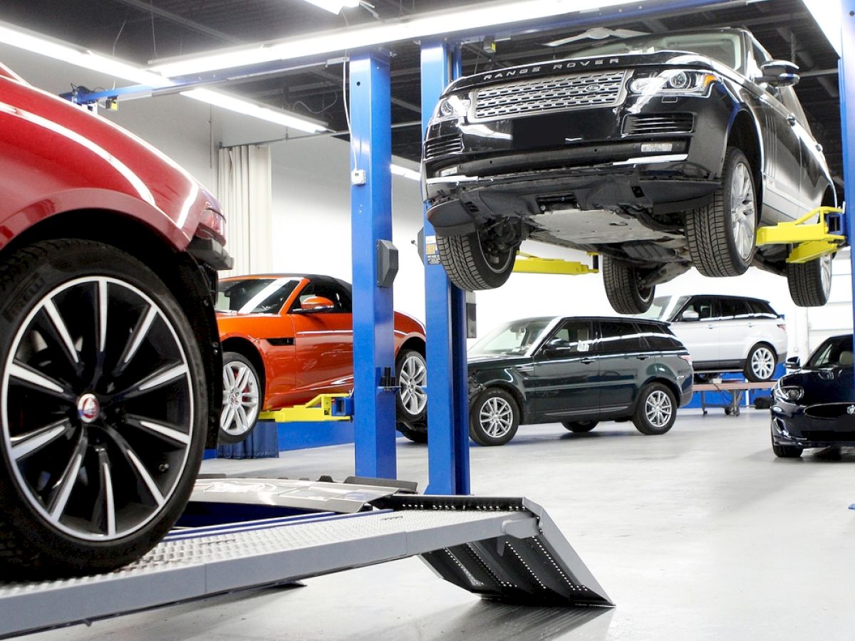 A car repair shop with multiple cars, some on lifts being serviced, in a brightly lit environment.