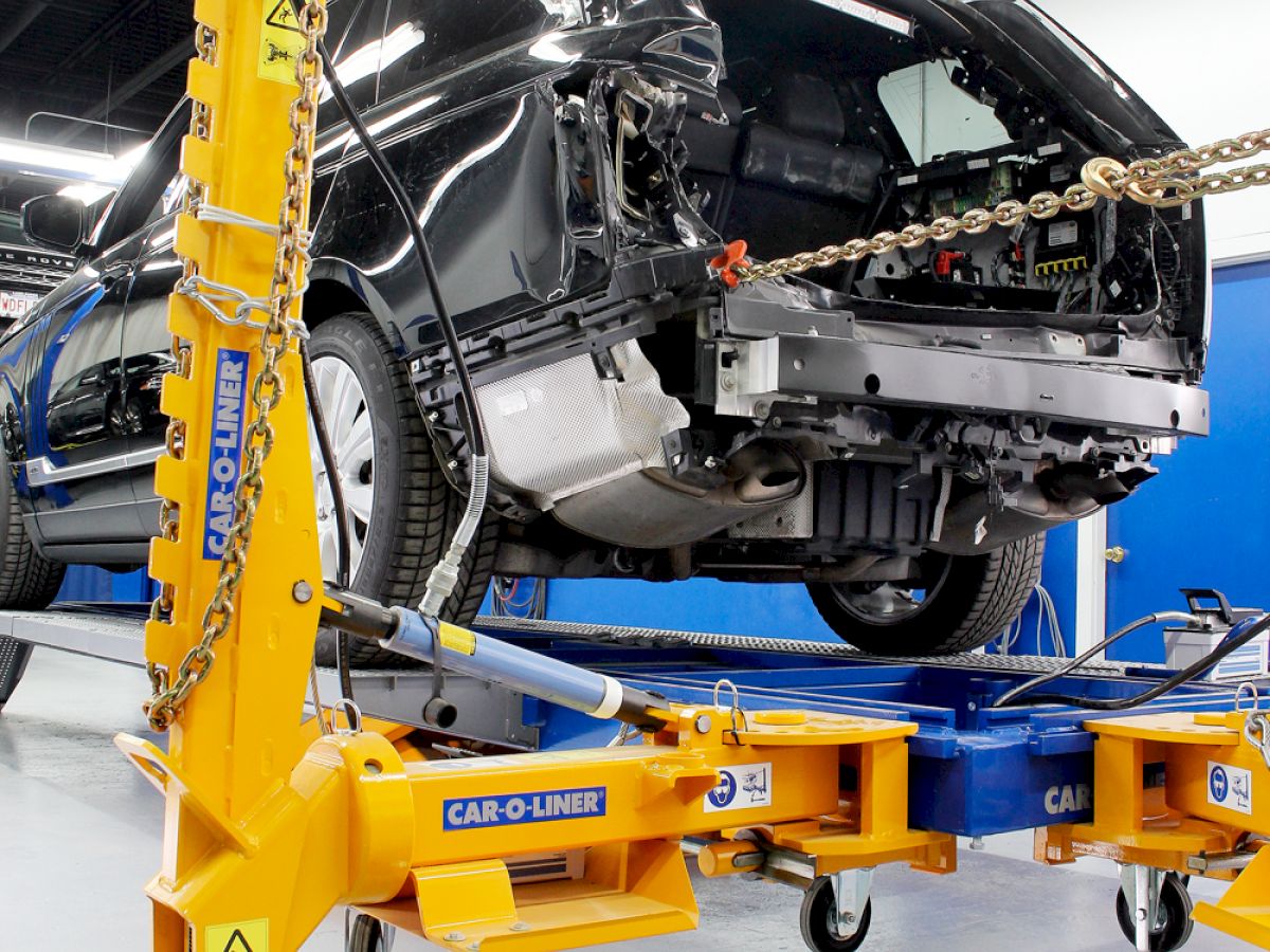 A car is elevated on a vehicle lift, with its front exposed and undergoing repairs in an auto repair shop.