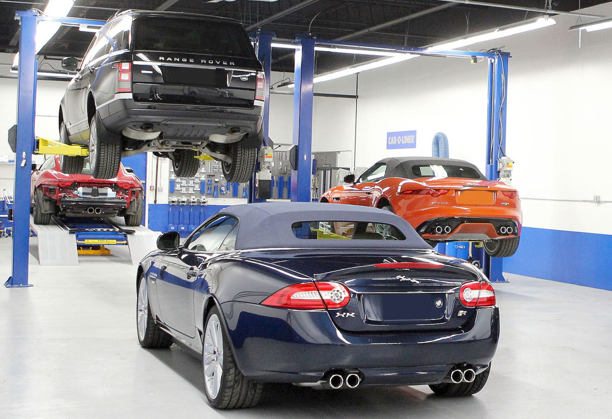 A car repair shop with several cars, including a convertible and an SUV on lifts, in a spacious, well-lit garage environment.