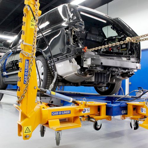 A partially disassembled vehicle is on a hydraulic lift in a workshop, equipped for repairs or maintenance, with tools and equipment nearby.
