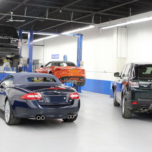 The image shows a car service garage with several vehicles, including a Range Rover and a convertible, some on lifts.