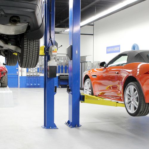 Two cars are lifted on hydraulic lifts in an auto repair shop, with tools and equipment in the background.