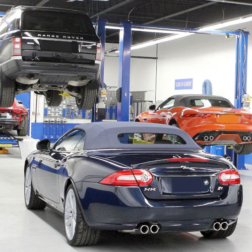A car repair garage with a black SUV and an orange sports car on lifts, and a blue convertible parked on the ground.