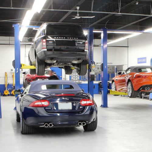 A car workshop with vehicles on lifts being serviced; several cars are visible, including a black SUV and a red sports car.